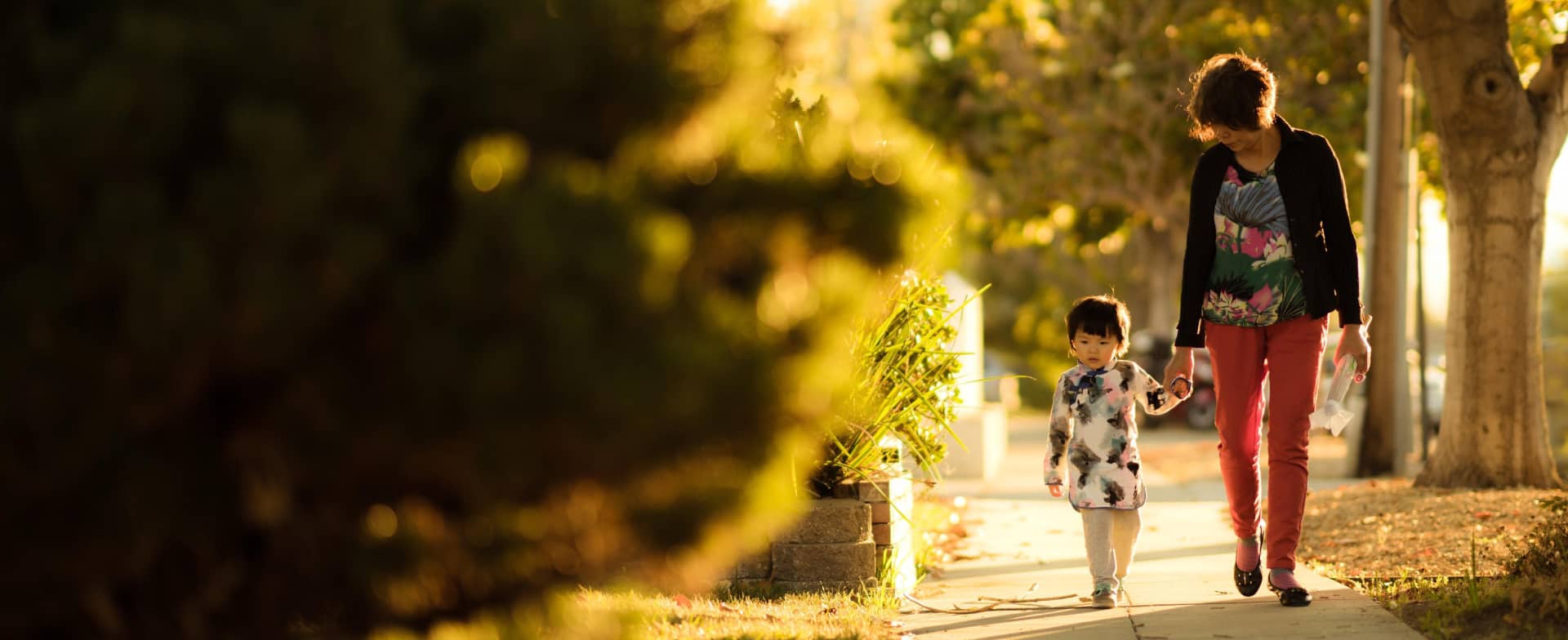 mother and child holding hands and walking down a sunny sidewalk